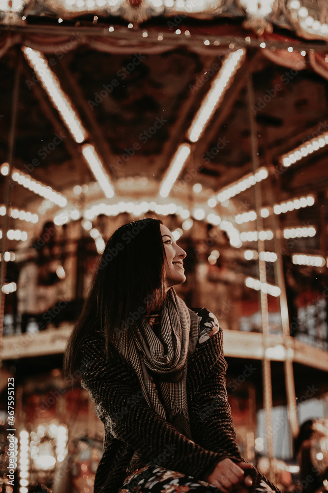 Young woman in cozy winter knitted grey scarf against the background of a gold sparkling carousel lights. New Year's and Christmas spirit. Winter mood and atmosphere
