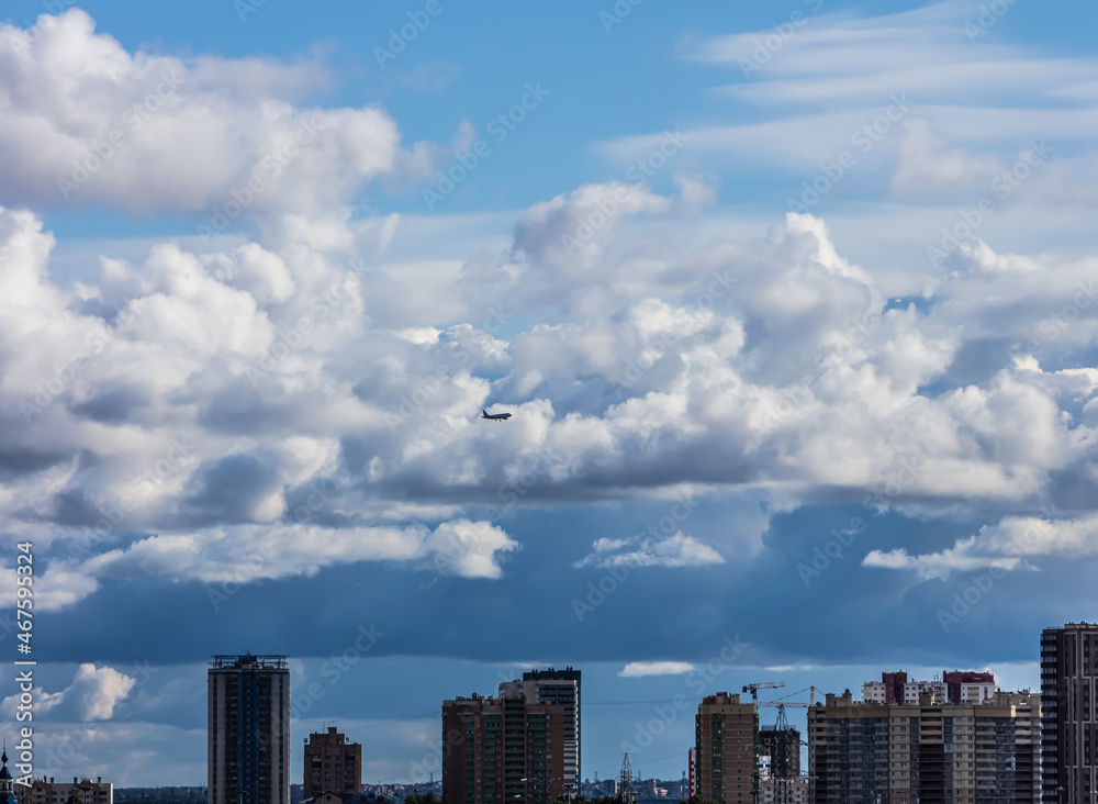 silhouette of an airplane flying over the city against the background of cumulus clouds