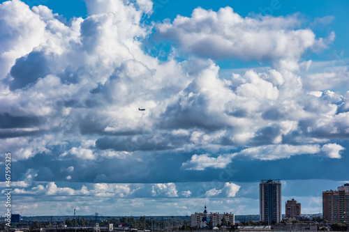 silhouette of an airplane flying over the city against the background of cumulus clouds © alexkazachok