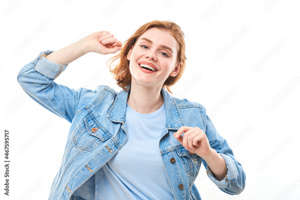 Obraz premium Young red-haired woman enjoys looking at the camera. Smiling girl in jeans on white background looking at camera