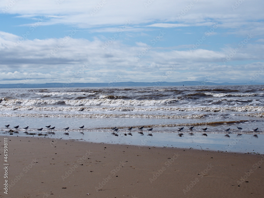 the beach at blundell flats in southport with waves braking on the beach and the wind turbines at burbo bank visible in the distance