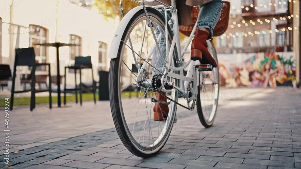 Back view of legs of unknown female who riding bike by city square. Autumn sunny day. Low angle tracking shot. Close up, slow motion