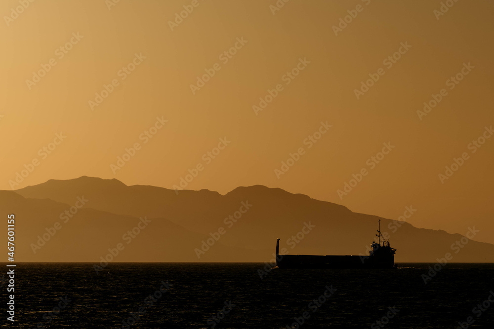 Fototapeta premium Cargo Ship at Sunset with Island in Background