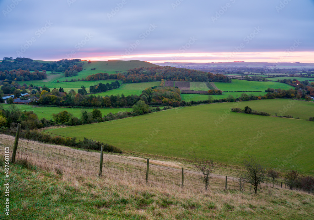 Naklejka premium beautiful morning sky as the sun rises over Giant's Grave and Oare village. View from South facing edge of the Marlborough Downs, Pewsey Vale, Wiltshire AONB 