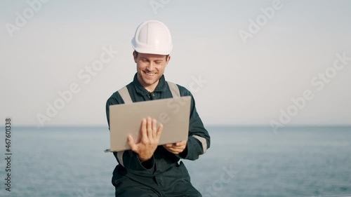 Young smiling sailor man standing on deck of vessel or ship and talking with family online on laptop