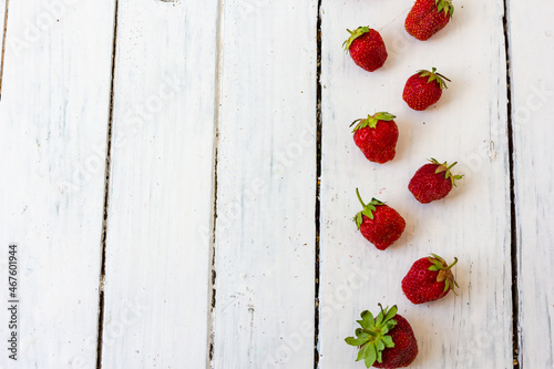 Ripe red strawberry lies in a pattern like a frame on a wooden white background. Copy space. View from above.
