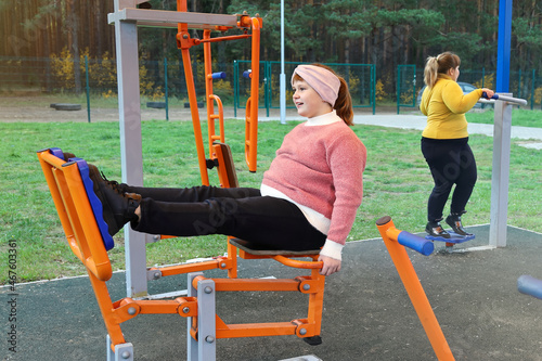Chubby girl performs sports exercises on street simulators outdoors