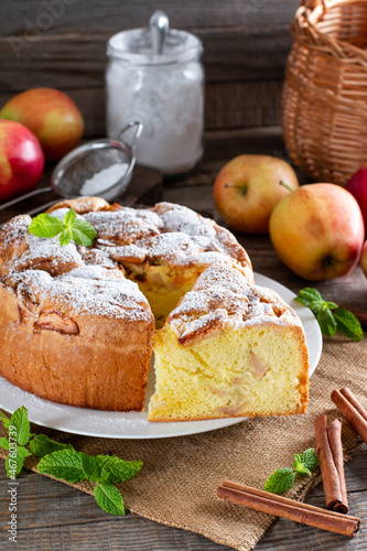Homemade round sponge cake or chiffon cake with apples on white plate so soft and delicious with ingredients: eggs, flour, milk on table. Homemade bakery concept for background and wallpaper.