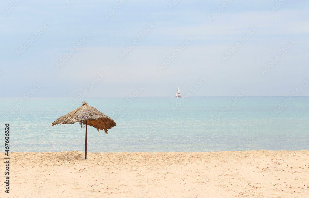 Straw beach umbrella on a tropical sandy beach on a background of blue sea on a sunny day.