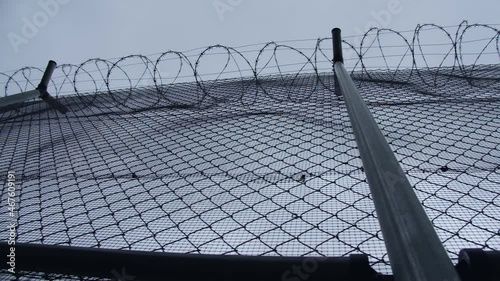 A chain-link fence with barbed wire of the prison or concentration camp with a grey cloudy sky backdrop photo