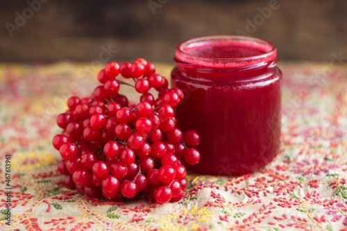 Bunch of viburnum berries, viburnum berry jam in a glass jar on an embroidered tablecloth. Preparations for the winter from a cold, Viburnum opulus