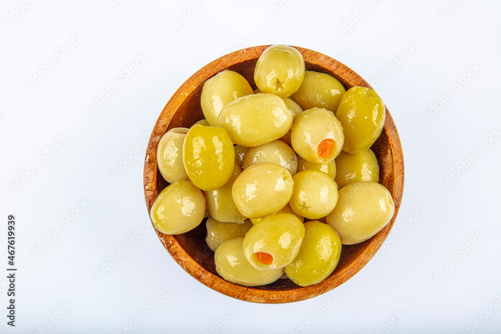 Pickled small green olives, filled with red sweet pepper in a wooden bowl. Fruits of Olea europaea, stuffed with bell pepper slices. Closeup from above, isolated on white background, macro food photo. Pickled small green olives, filled with red sweet pepper in a wooden bowl. Fruits of Olea europaea, stuffed with bell pepper slices. Closeup from above, isolated on white background, macro food photo.