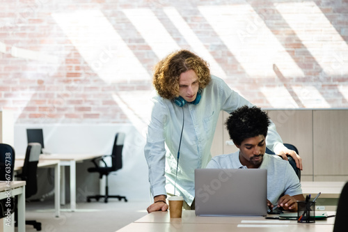 Young multiracial coworkers look at laptop together brainstorming ideas for business. Copy space.