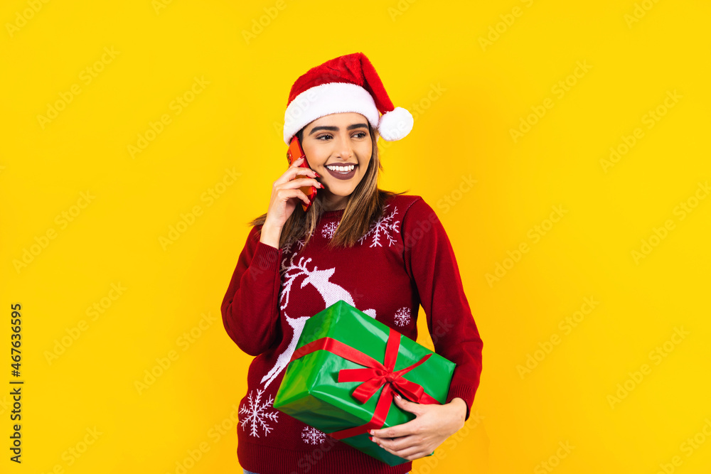 Portrait of Latin woman holding Christmas gift box and calling by mobile phone on a yellow background in Mexico latin america Portrait of Latin woman holding Christmas gift box and calling by mobile phone on a yellow background in Mexico latin america
