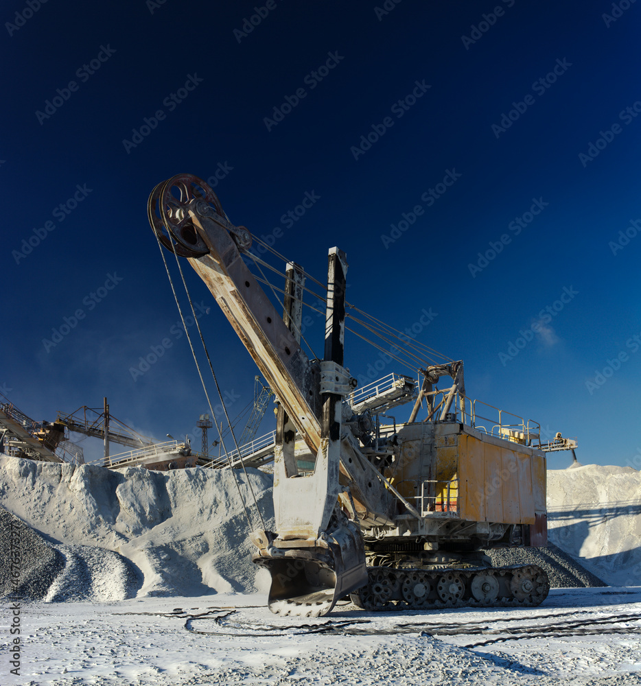 Obraz premium Heavy quarry excavator against the background of dark blue sky in a winter sunny day, panorama.