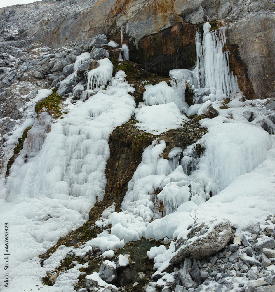 Beautiful texture of the stone surface in winter cloudy day with a layer of ice from behind a spring flowing out of the cliff, close-up panorama. Beautiful texture of the stone surface in winter cloudy day with a layer of ice from behind a spring flowing out of the cliff, close-up panorama.