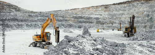 Panorama of a limestone quarry with heavy mining machinery - hydraulic hammer, excavator and drilling rig, on a cloudy winter day.