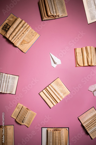 books on pink wall with paper planes and open books