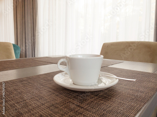 A white cup of tea with a saucer is on the table, behind is a window. Copspace