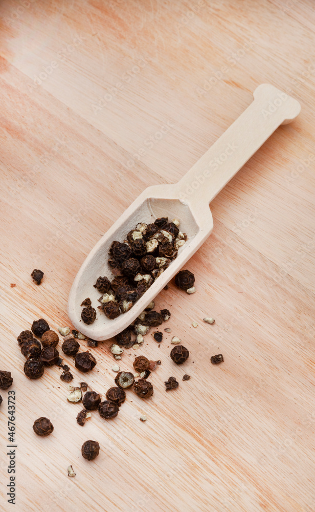 black peppercorns on wooden surface with tiny scoop black peppercorns on wooden surface with tiny scoop