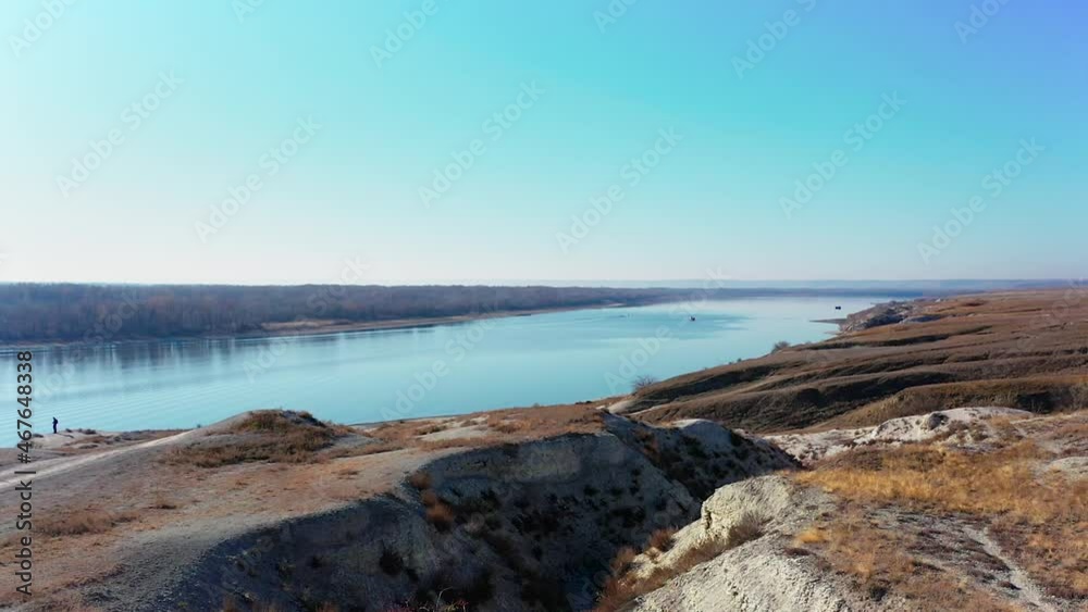 Hilly terrain with crevices and a river, captured by smooth movement at low altitude with the image of an abstract operator in sight. Hilly terrain with crevices and a river, captured by smooth movement at low altitude with the image of an abstract operator in sight.