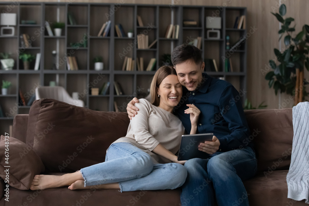 Happy couple hugging, using tablet together, relaxing on couch, smiling  wife and husband looking at electronic device screen, watching funny video  or chatting online, spending leisure time at home Stock Photo |