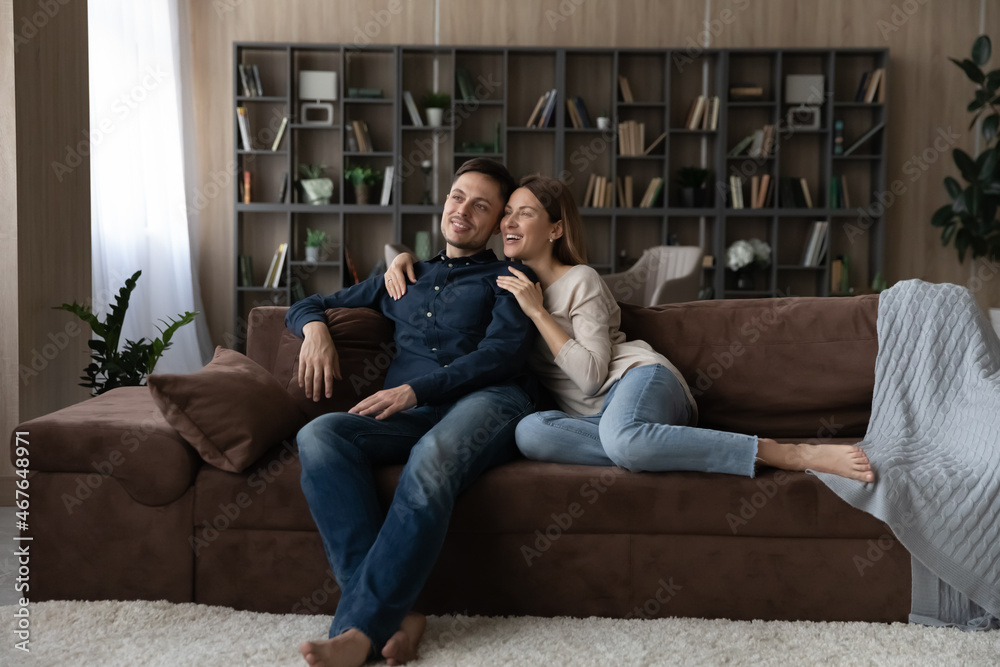 Happy dreamy Caucasian loving couple hugging, relaxing sitting on couch at home, smiling wife and husband looking to aside, dreaming of good future, new opportunities together, enjoying weekend Happy dreamy Caucasian loving couple hugging, relaxing sitting on couch at home, smiling wife and husband looking to aside, dreaming of good future, new opportunities together, enjoying weekend