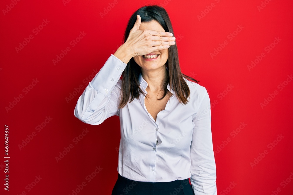 Young hispanic woman wearing business shirt and glasses smiling and laughing with hand on face covering eyes for surprise. blind concept. Young hispanic woman wearing business shirt and glasses smiling and laughing with hand on face covering eyes for surprise. blind concept.