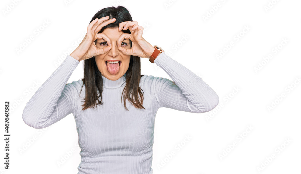 Beautiful brunette woman wearing casual clothes doing ok gesture like binoculars sticking tongue out, eyes looking through fingers. crazy expression. Beautiful brunette woman wearing casual clothes doing ok gesture like binoculars sticking tongue out, eyes looking through fingers. crazy expression.