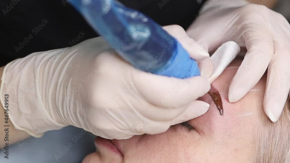 The master makes permanent eyebrow makeup with a needle tattoo machine The master makes permanent eyebrow makeup with a needle tattoo machine