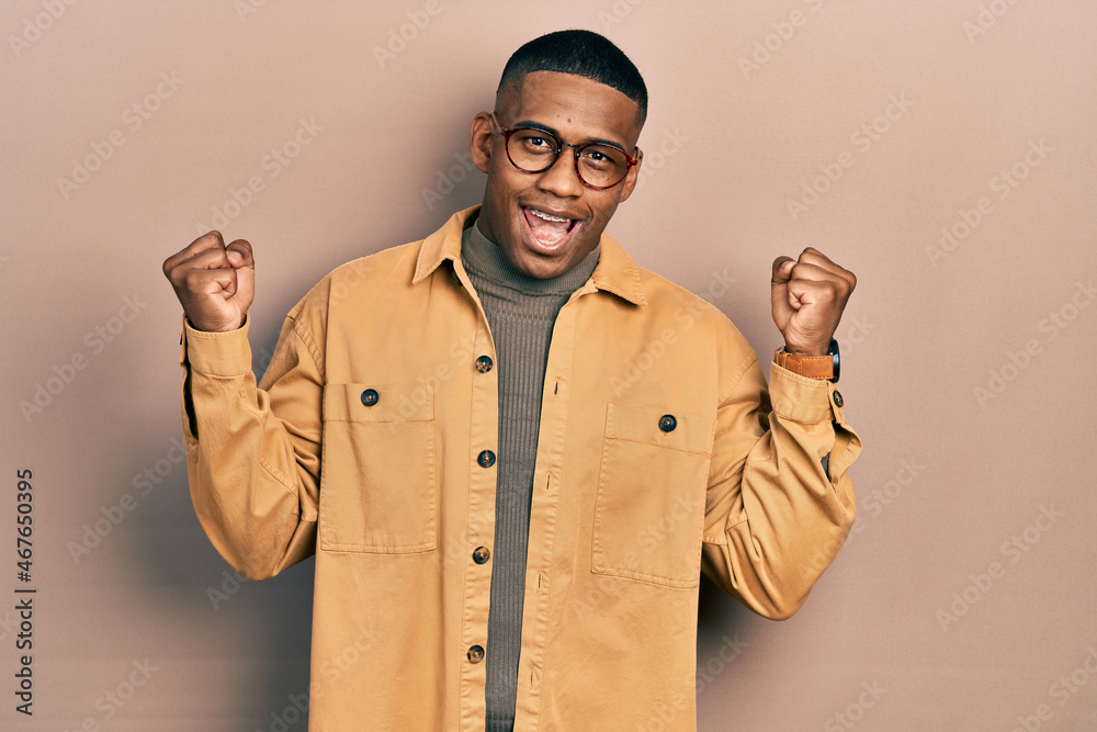Young black man wearing casual clothes and glasses screaming proud, celebrating victory and success very excited with raised arms Young black man wearing casual clothes and glasses screaming proud, celebrating victory and success very excited with raised arms