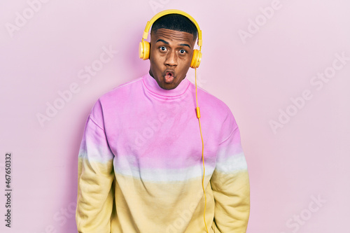 Young black man listening to music wearing headphones afraid and shocked with surprise expression, fear and excited face.
