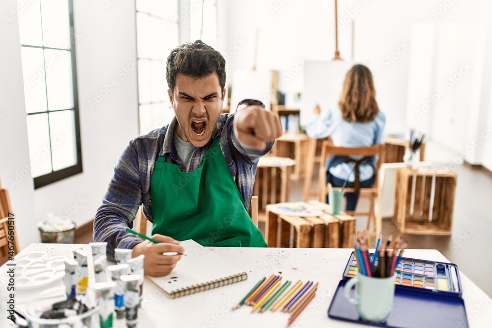 Young artist man at art studio pointing displeased and frustrated to the camera, angry and furious with you