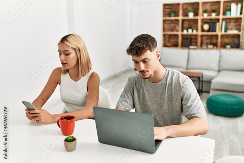Young caucasian couple drinking coffee and using laptop and smartphone at home.