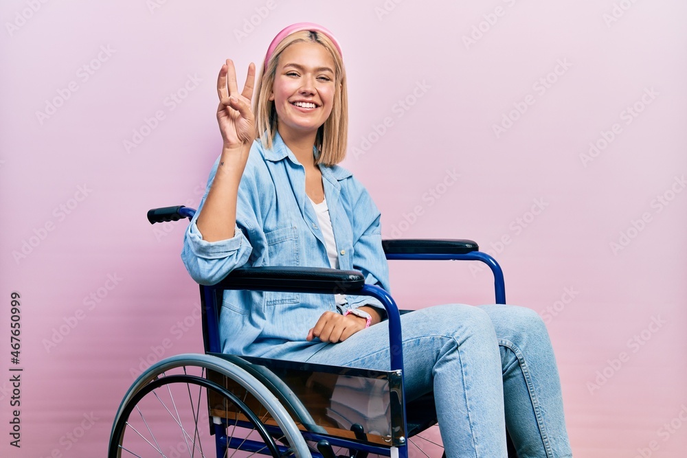 Beautiful blonde woman sitting on wheelchair showing and pointing up with fingers number three while smiling confident and happy. Beautiful blonde woman sitting on wheelchair showing and pointing up with fingers number three while smiling confident and happy.