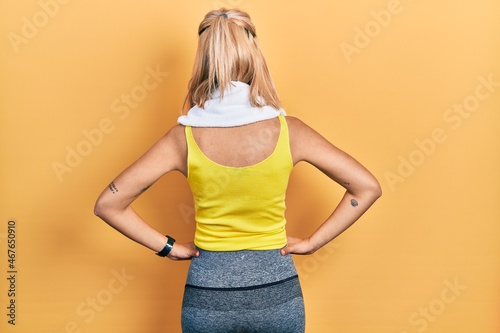 Beautiful blonde sports woman wearing workout outfit standing backwards looking away with arms on body