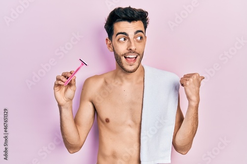 фотографія Young hispanic man standing shirtless holding razor pointing thumb up to the sid