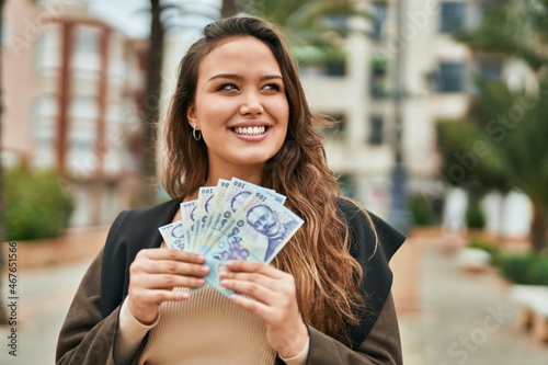 Young hispanic woman smiling happy holding romania leu banknotes at the city.