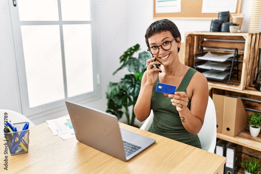 Young hispanic woman talking on the smartphone using credit card at office Young hispanic woman talking on the smartphone using credit card at office