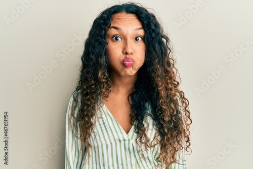 Young latin woman wearing casual clothes puffing cheeks with funny face. mouth inflated with air, crazy expression.