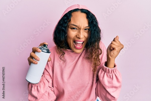 Young latin woman wearing sweatshirt holding graffiti spray screaming proud  celebrating victory and success very excited with raised arms