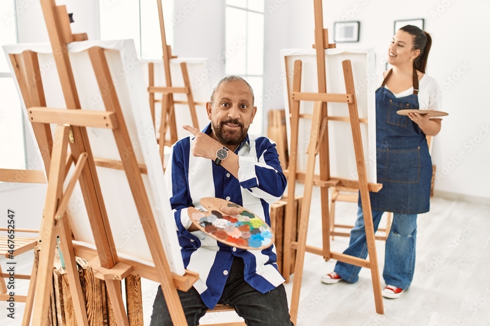 Senior artist man at art studio cheerful with a smile on face pointing with hand and finger up to the side with happy and natural expression
