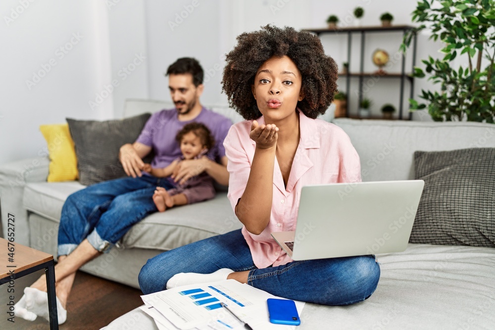 Mother of interracial family working using computer laptop at home looking at the camera blowing a kiss with hand on air being lovely and sexy. love expression. Mother of interracial family working using computer laptop at home looking at the camera blowing a kiss with hand on air being lovely and sexy. love expression.