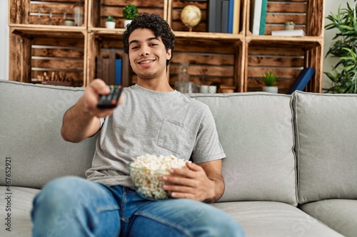 Young hispanic man watching movie sitting on the sofa at home.