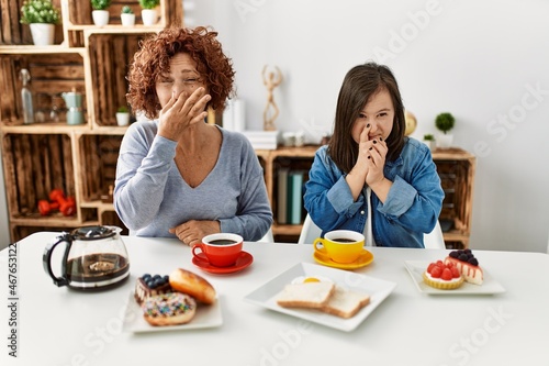 Family of mother and down syndrome daughter sitting at home eating breakfast smelling something stinky and disgusting  intolerable smell  holding breath with fingers on nose. bad smell