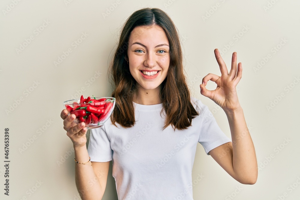 Young brunette woman holding red peppers doing ok sign with fingers, smiling friendly gesturing excellent symbol Young brunette woman holding red peppers doing ok sign with fingers, smiling friendly gesturing excellent symbol