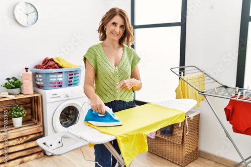 Cuadro en lienzo Middle age woman ironing clothes at home smiling happy pointing with hand and fi