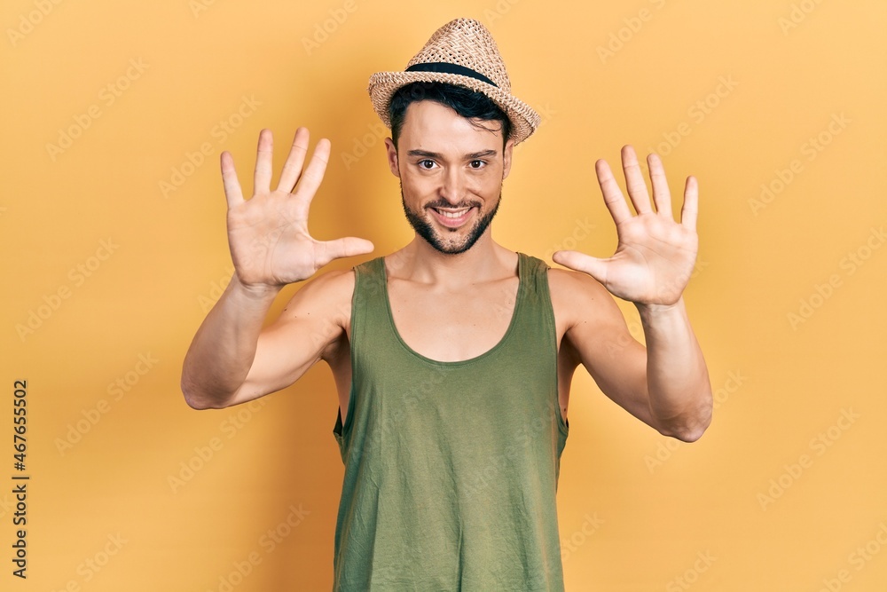 Naklejka premium Young hispanic man wearing summer hat showing and pointing up with fingers number ten while smiling confident and happy.