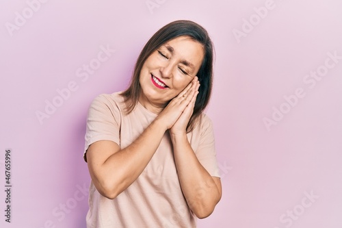 Middle age hispanic woman wearing casual clothes sleeping tired dreaming and posing with hands together while smiling with closed eyes.
