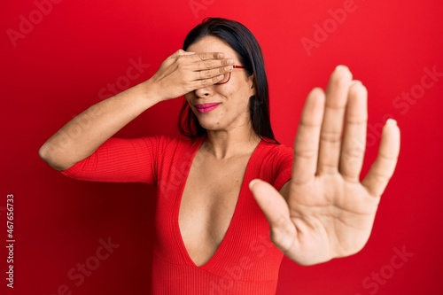 Young latin woman wearing casual clothes and glasses covering eyes with hands and doing stop gesture with sad and fear expression. embarrassed and negative concept. © Krakenimages.com